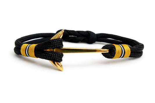 Tropical Vibes Co. nautical bracelet featuring a double-strand black braided cord, vibrant yellow and white accent thread wraps, and a polished gold-finished anchor clasp centered on a clean white background